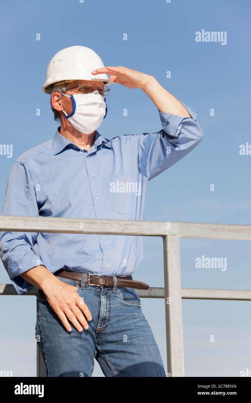 Ingenieur oder Architekt mit Hut und chirurgische Maske wegen covid-19 auf der Suche nach einer besseren Zukunft Stockfoto