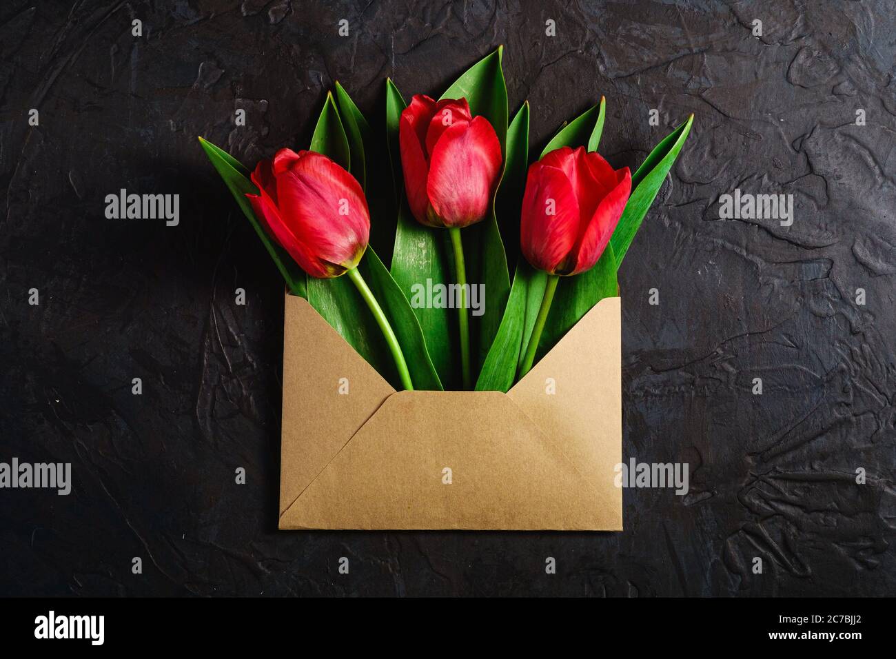 Bündel von roten Tulpen Blumen in Papier Umschlag auf strukturiertem dunklen schwarzen Hintergrund, Ansicht von oben Kopierraum Stockfoto