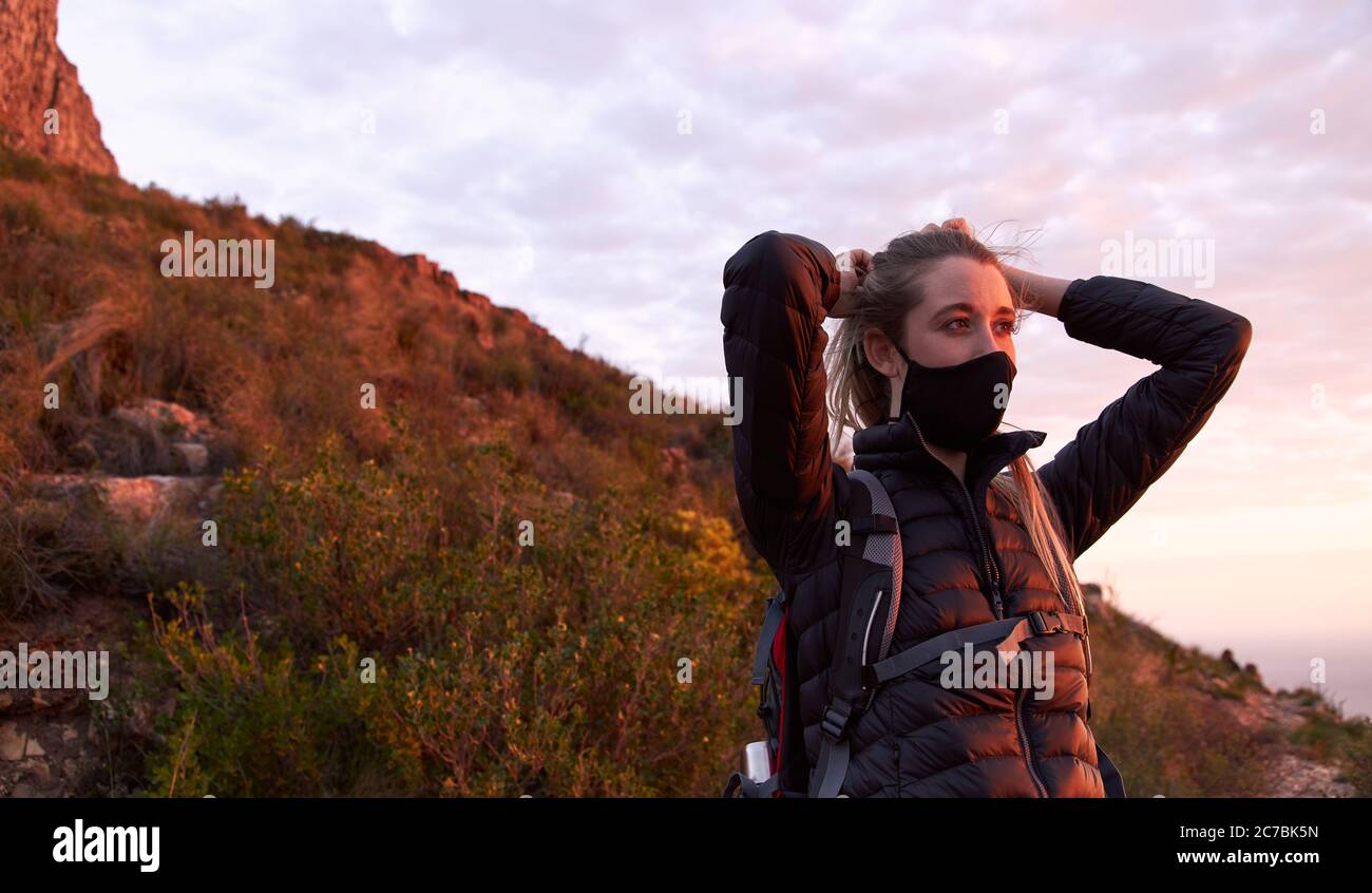 Junge Frau Anpassung Gesichtsmaske auf der Spitze des Berges während des Sonnenuntergangs Stockfoto