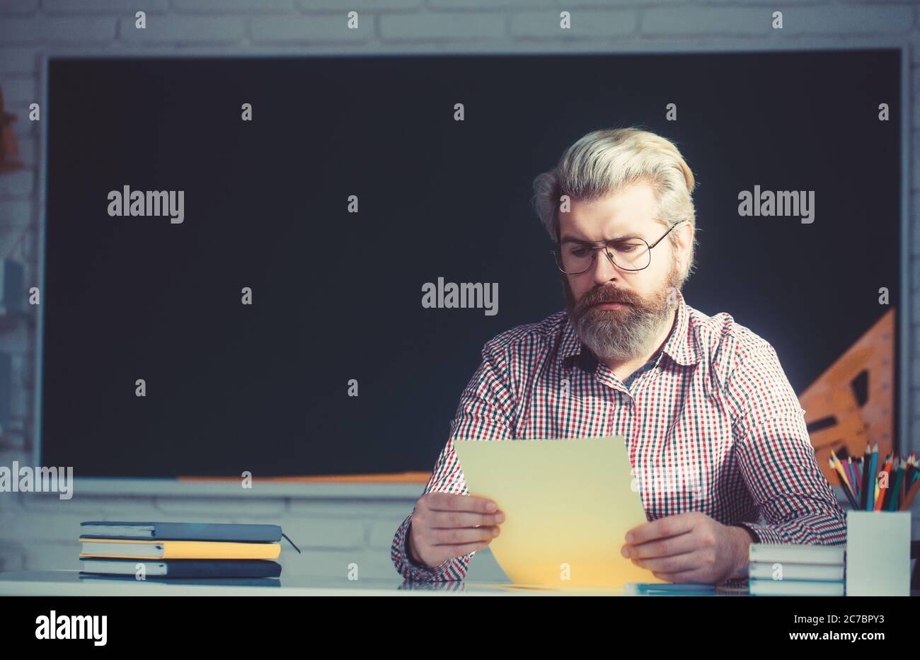 Schöner männlicher Lehrer Überprüfung Hausaufgaben im Klassenzimmer. Stockfoto