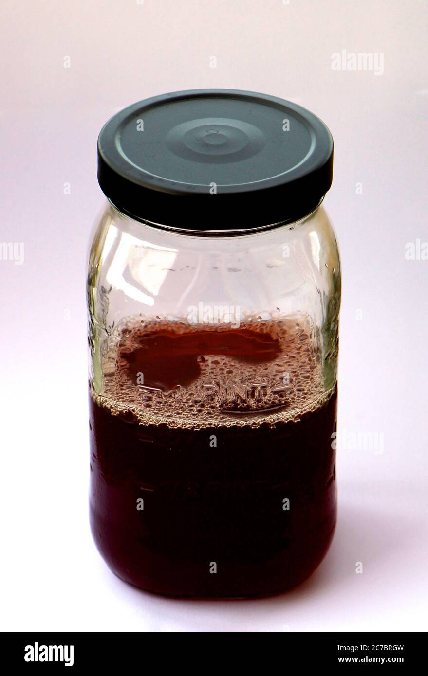 Versiegeltes Klarglas-Messglas mit vier Messmethoden und einem schwarzen Metalldeckel mit dunkelrotem Waldfruchtsaft halb voll oder halb leer Pint Stockfoto