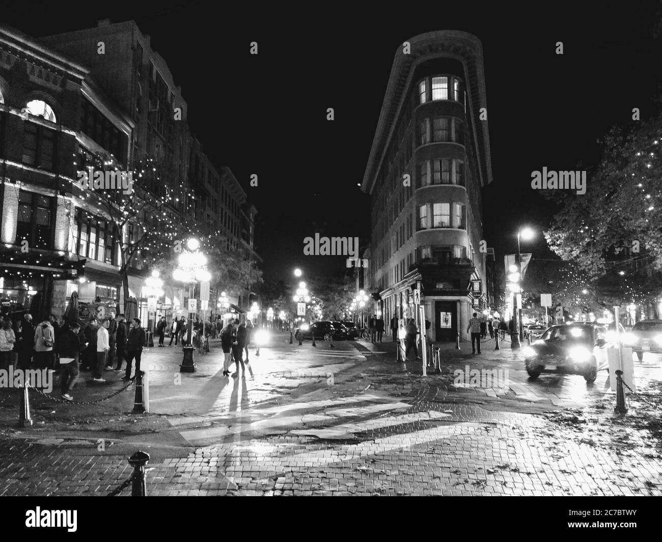 Graustufen horizontale Aufnahme eines Stadtzentrums während der Nacht Mit Autos und Menschen vorbei Stockfoto