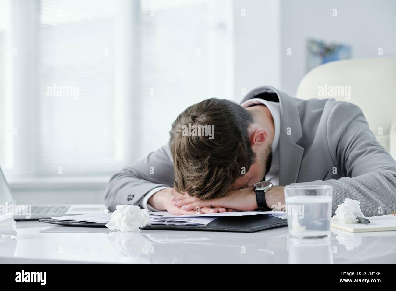 Erschöpfter junger Geschäftsmann liegt mit Papieren und zerknitterte Servietten auf dem Tisch und leidet Kopfschmerzen Stockfoto