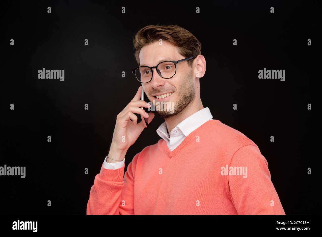 Lächelnd selbstbewusst junger Mann in hellen Pullover mit Telefongespräch vor schwarzem Hintergrund Stockfoto