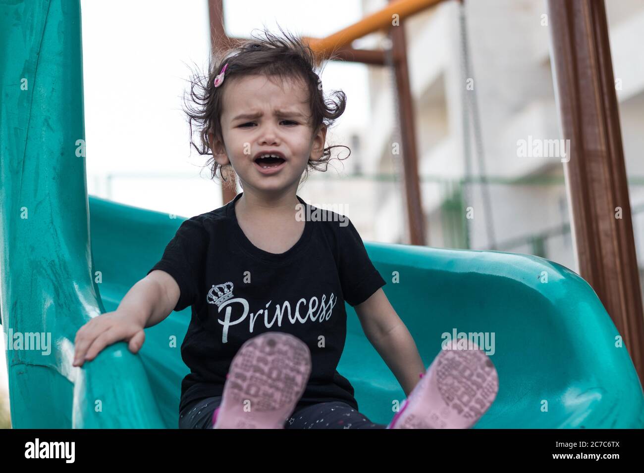 Ein launisch kleines Mädchen auf einer Rutsche auf einem Spielplatz. Stockfoto