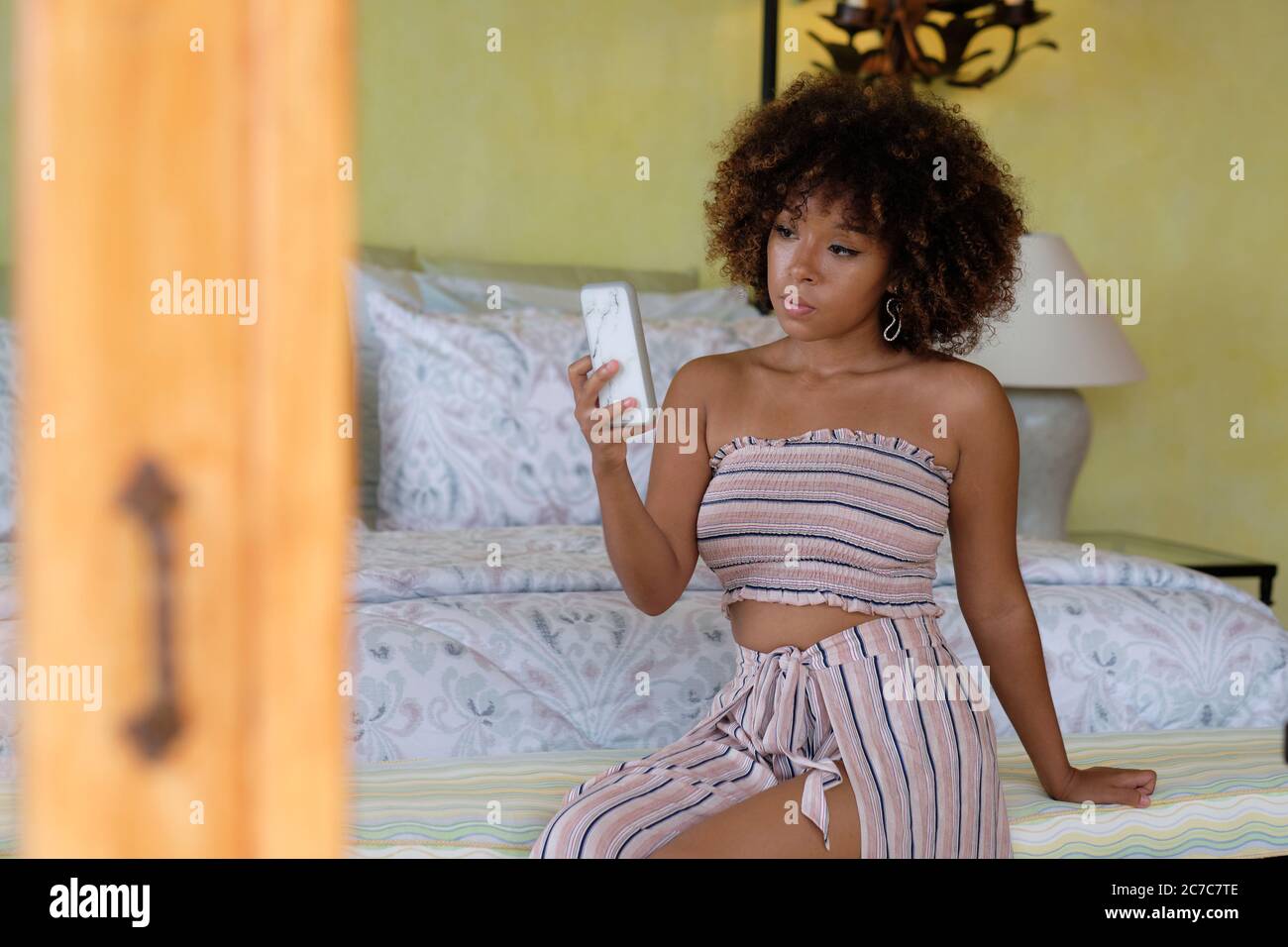 Junge Frau mit afro-Look Haare überprüfen ihr Telefon oder ein Selfie in einem Schlafzimmer Stockfoto
