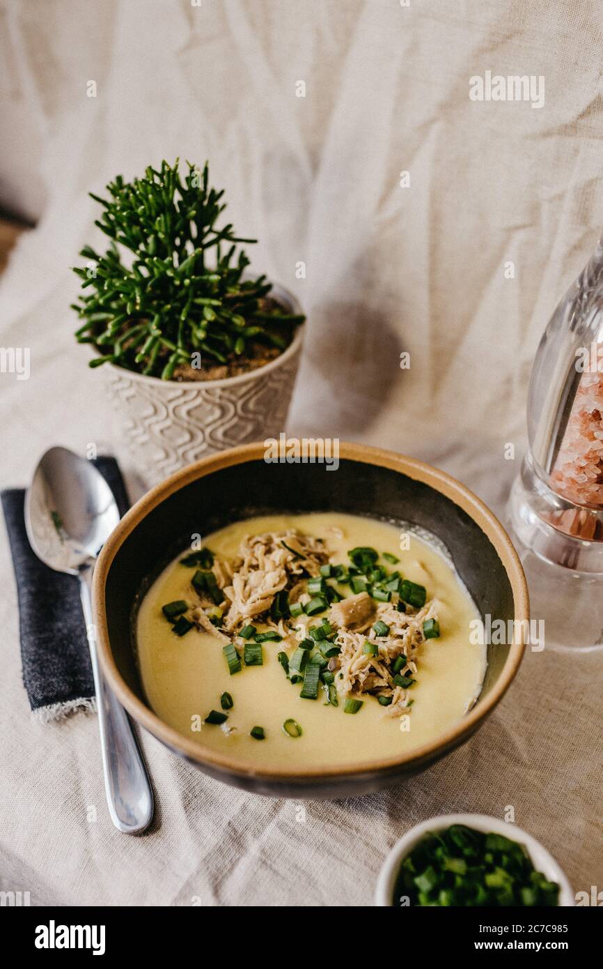 Vertikale Aufnahme einer schwarzen Schüssel voller Suppe auf Ein Tisch mit einer Pflanze daneben Stockfoto