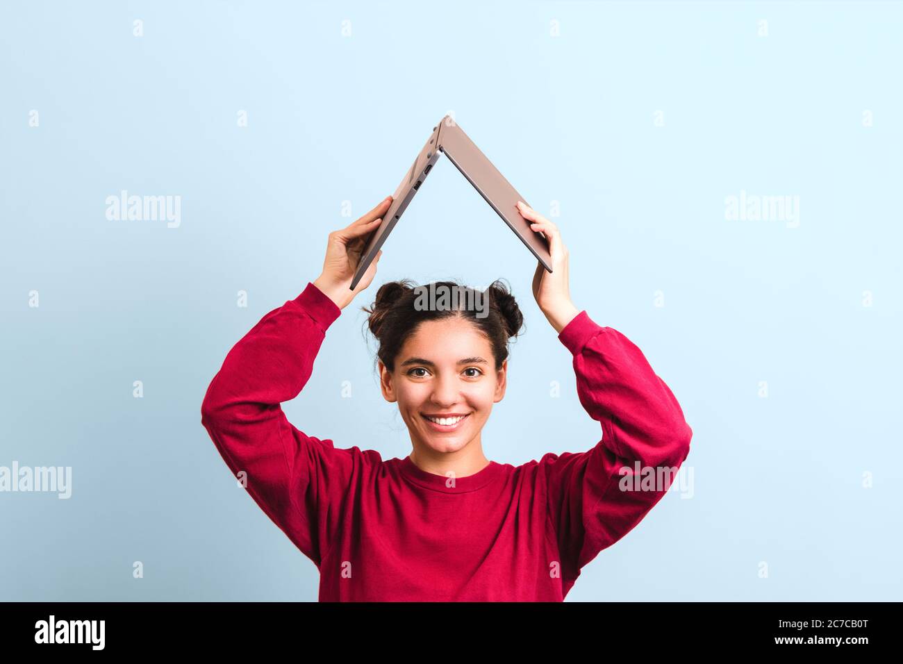 Junge fröhliche Frau Student mit schönen Lächeln hält einen geöffneten Laptop über den Kopf in Form von Dach. Investieren in Bildung Stockfoto