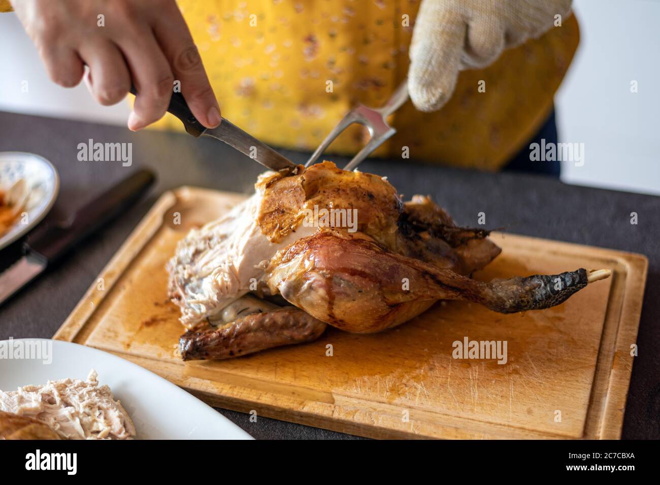 Kaukasische Frau, die ein gebratenes Huhn auf einer Holzplatte mit einem Messer und einer Gabel schnitzt. Stockfoto