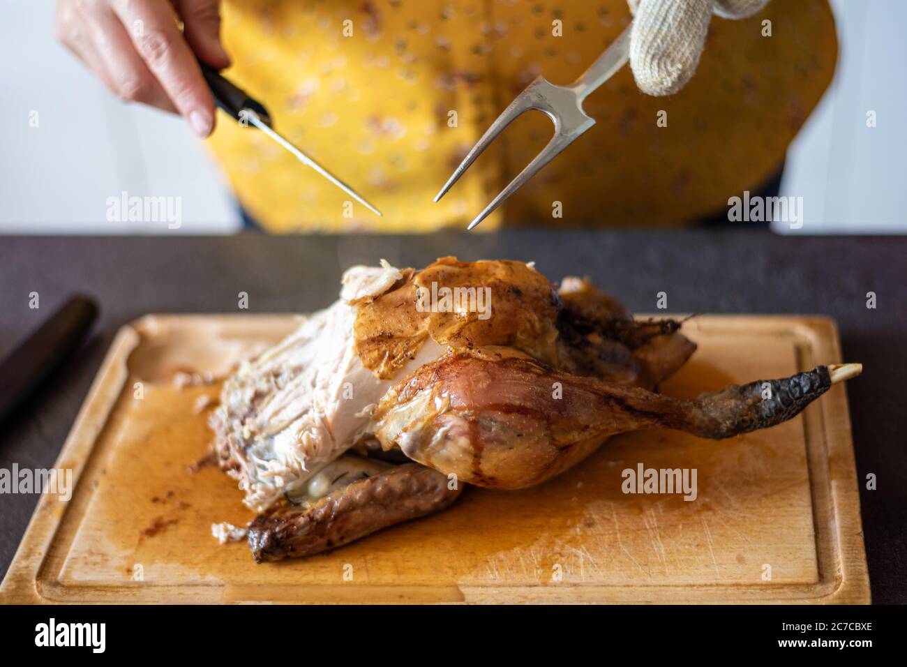 Kaukasische Frau, die ein gebratenes Huhn auf einer Holzplatte mit einem Messer und einer Gabel schnitzt. Stockfoto