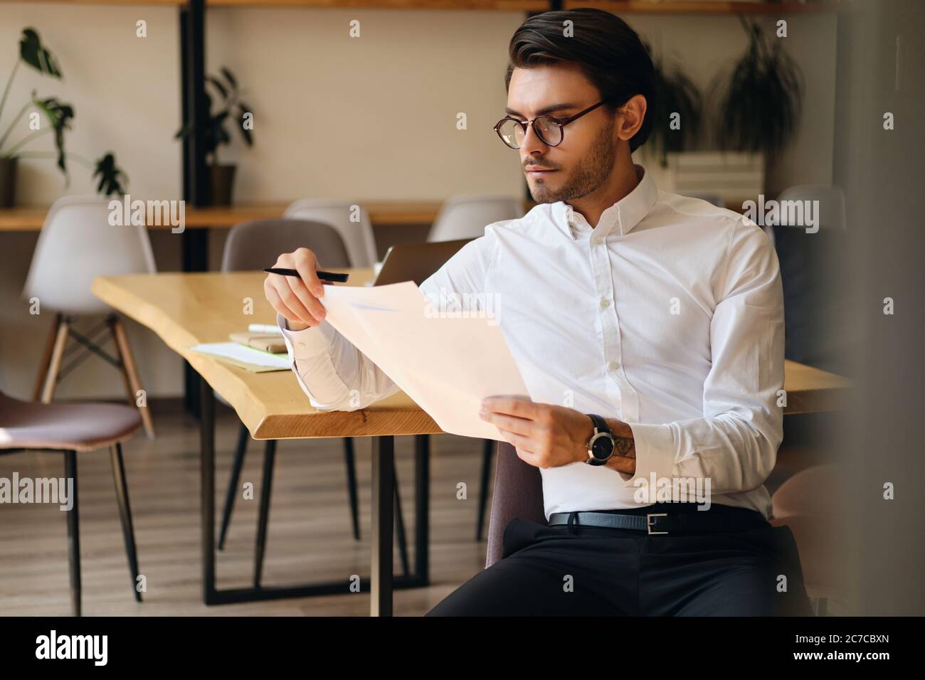 Junger seriöser Geschäftsmann in Brillen nachdenklich mit Papieren im Büro arbeiten Stockfoto
