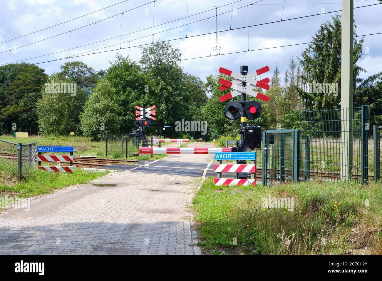Bahnübergang mit geschlossenen Barrieren und blinkenden roten Lichtern. Blaues Warnschild holländischer Text, warten bis rotes Licht verschwunden ist, Möglichkeit von anderem Zug Stockfoto