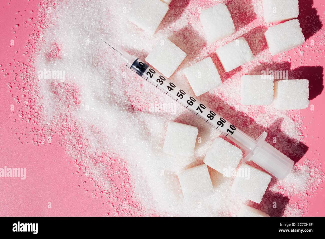Granulatzucker, Zuckerwürfel und Spritze auf rosa Backgroud. Stockfoto