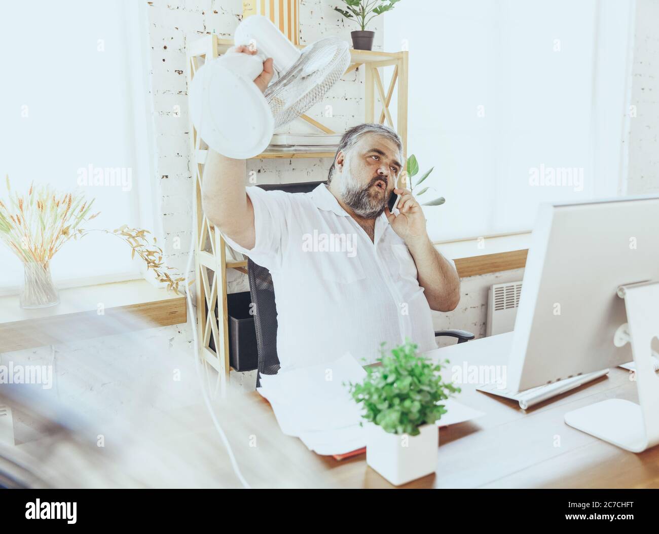 Extrem. Geschäftsmann, Manager im Büro mit Computer und Ventilator, der sich abkühlt, heiß fühlt, gespült. Mit Ventilator, aber immer noch leiden von unbequem Klima im Schrank. Sommer, Büroarbeit, Business. Stockfoto