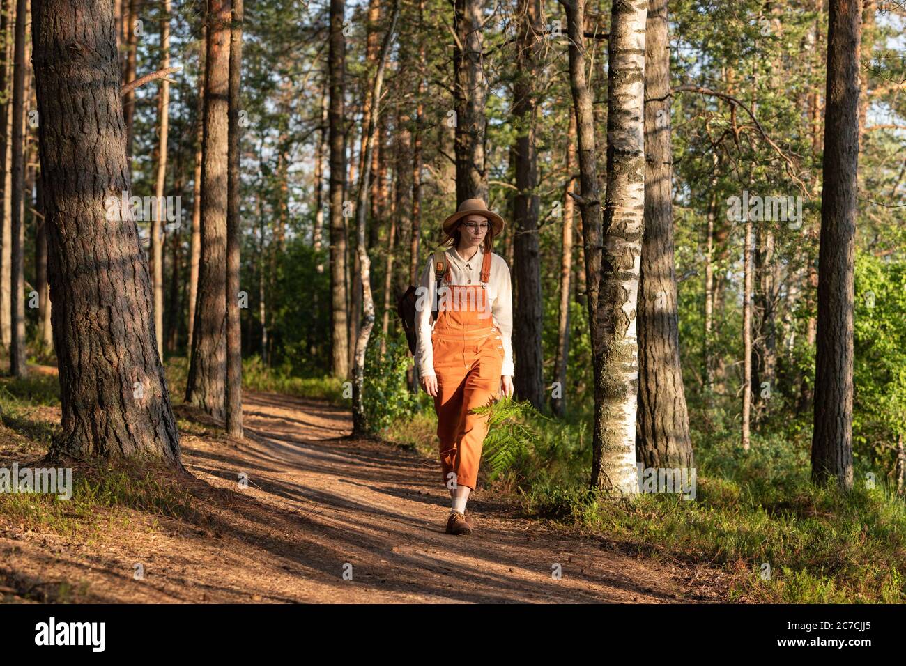 Frau Botanikerin in orange Overalls mit Rucksack auf ökologischen Wanderweg im Wald. Naturforscher erkunden Tierwelt und Ökotourismus Abenteuer Wandern i Stockfoto
