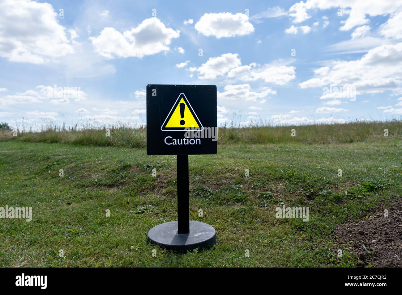 Ein gelbes Warnschild in einem grünen Feld unter einem blauen Himmel. Ökologie, Umweltwarnung. Stockfoto