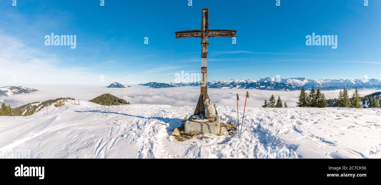 Gipfelkreuz auf Schneeberg mit blauem Himmel und toller Aussicht auf die Bergkette über der Talnebelschicht. Rucksack und Wanderstöcke. Rangiswanger Horn Stockfoto