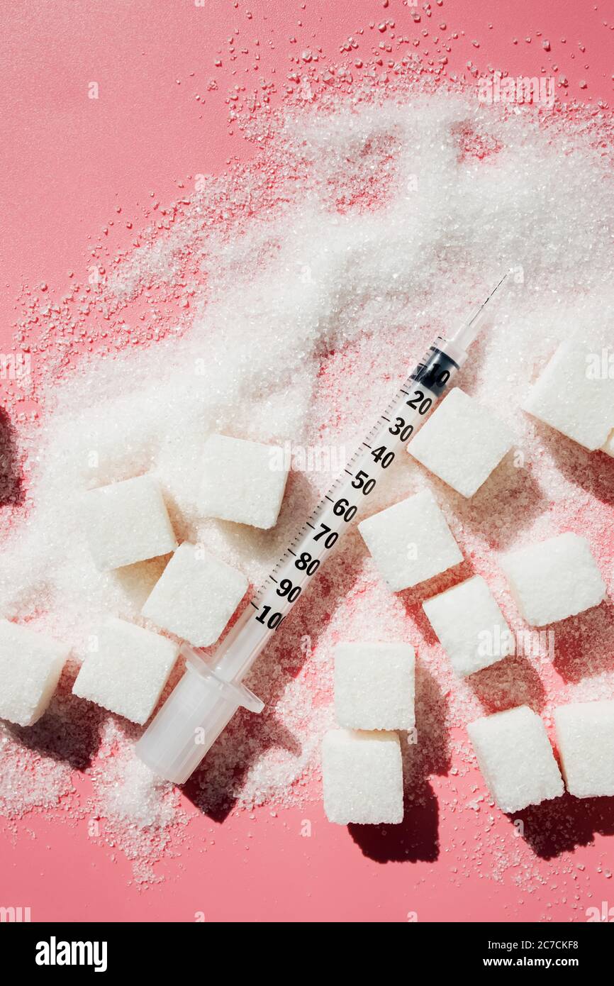 Granulatzucker, Zuckerwürfel und Spritze auf rosa Backgroud. Stockfoto