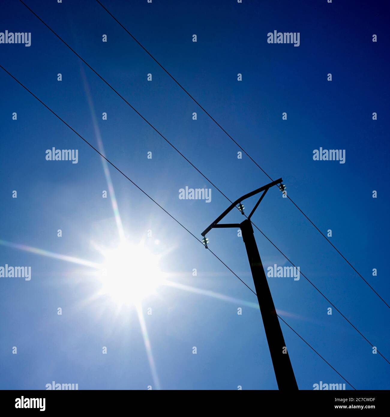 Helles Sonnenlicht, das über einem Strommast gegen einen klaren blauen Himmel während des Mittags in Frankreich leuchtet Stockfoto