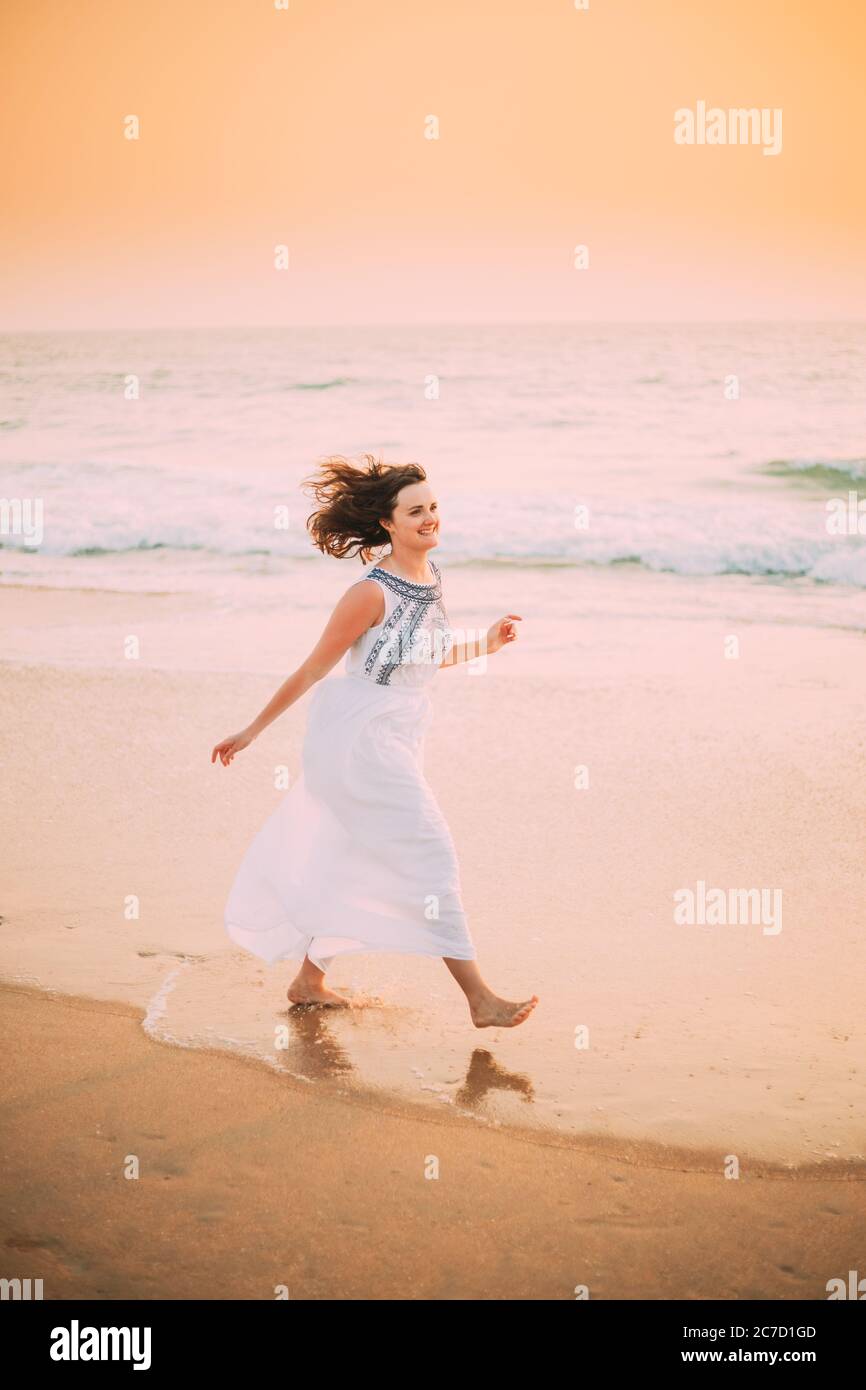 Goa, Indien. Junge Kaukasische Frau Mit Flatternden Haaren Im Wind In Weißem Kleid Wandern Entlang Der Küste, Genießen Sie Das Leben Und Lächeln Im Sommer Sonnenlicht Stockfoto