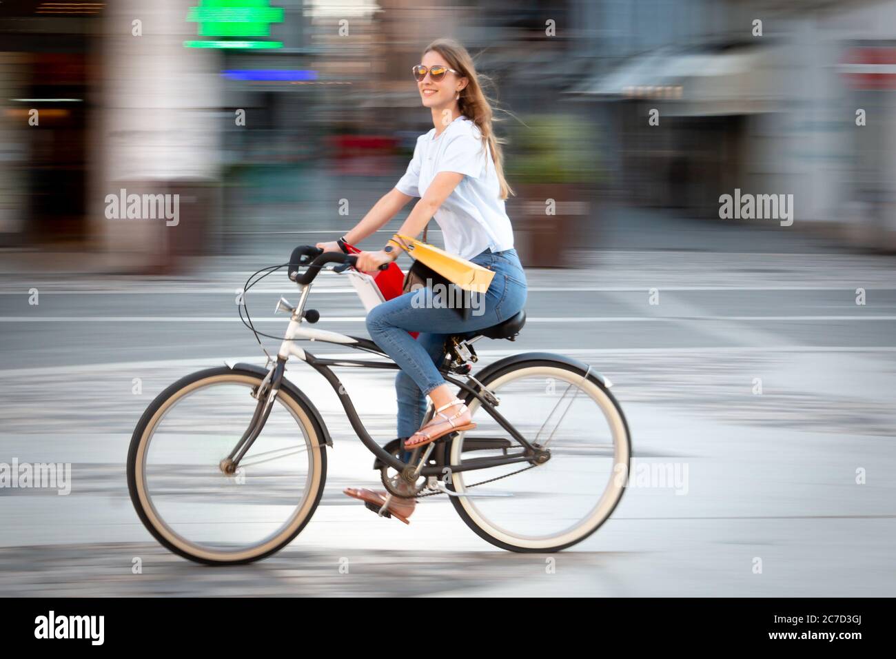 Schwenken eines schönen Mädchen tun Fahrrad einkaufen - bewegendes Foto eines Mädchens Reiten ein Fahrrad mit Einkaufstaschen Stockfoto