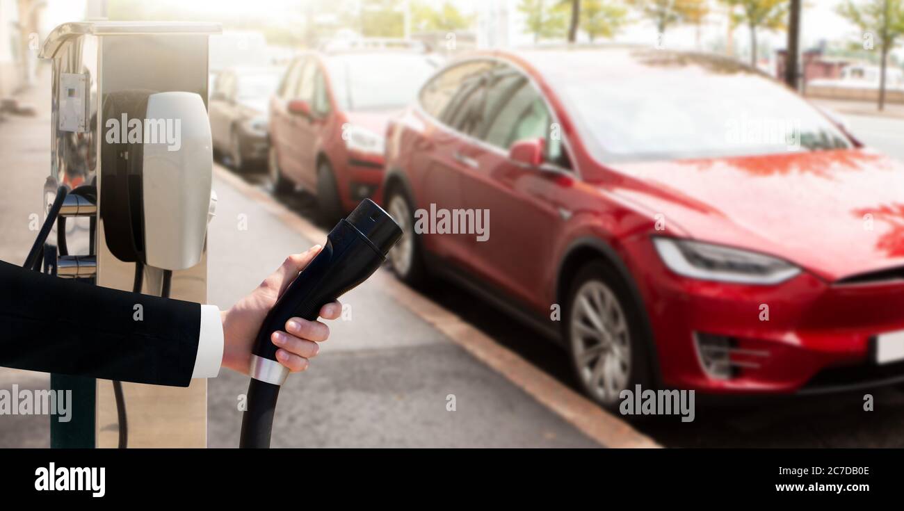 Hand mit Ladegerät auf einem Hintergrund von Elektroauto Stockfoto