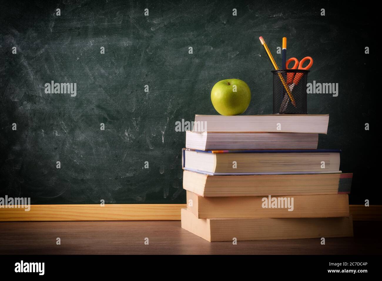 Stapel von Büchern mit Bleistift und Apfel auf Klassentisch mit grüner Kreidetafel im Hintergrund. Konzept des Studiums. Stockfoto