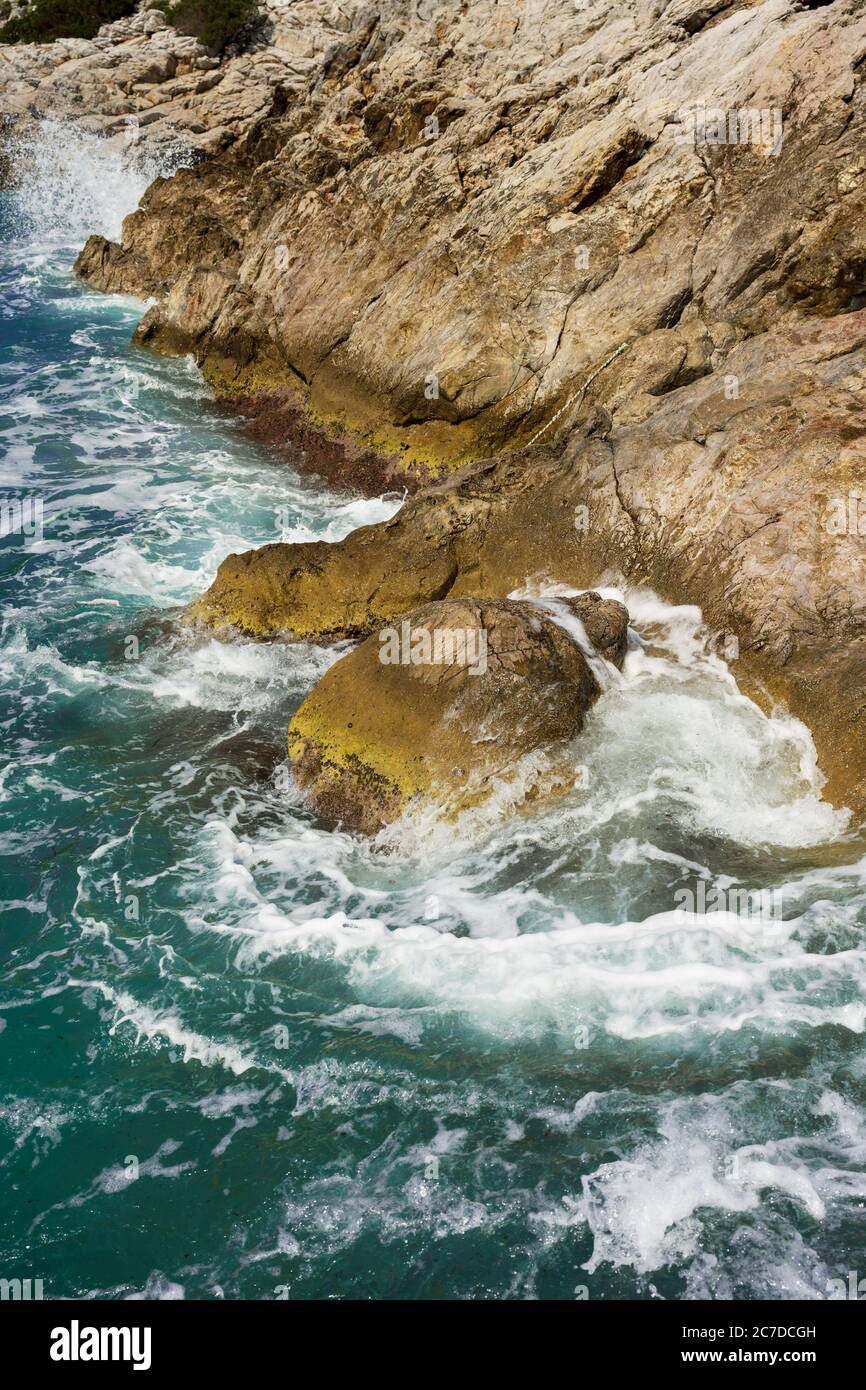 Wellen des blauen Meeres brechen schäumend an warmen farbigen Felsen. Stockfoto