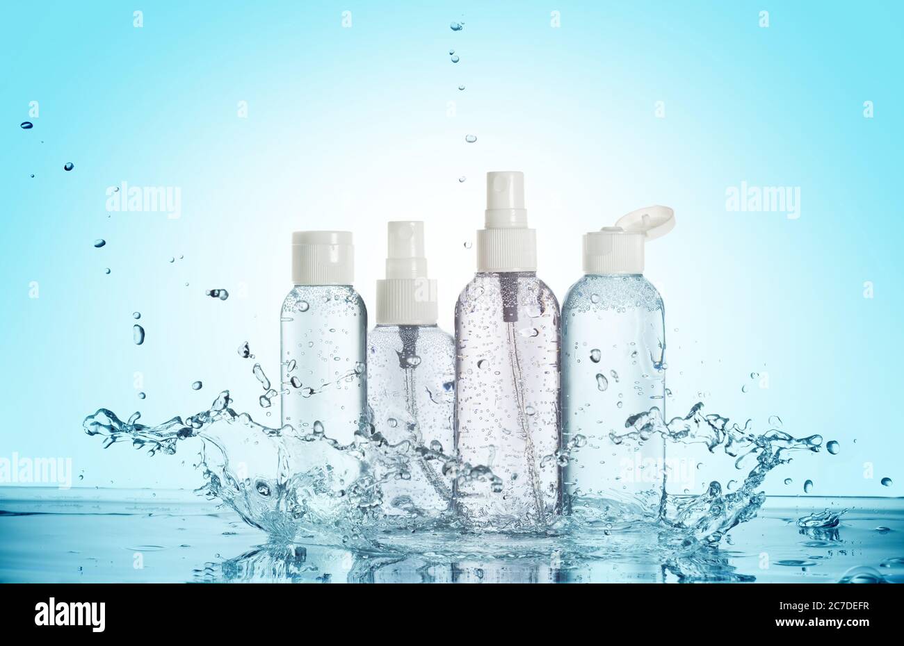 Flaschen von Beauty-Produkten in einem Wasserspritzer isoliert auf blauem Hintergrund Stockfoto