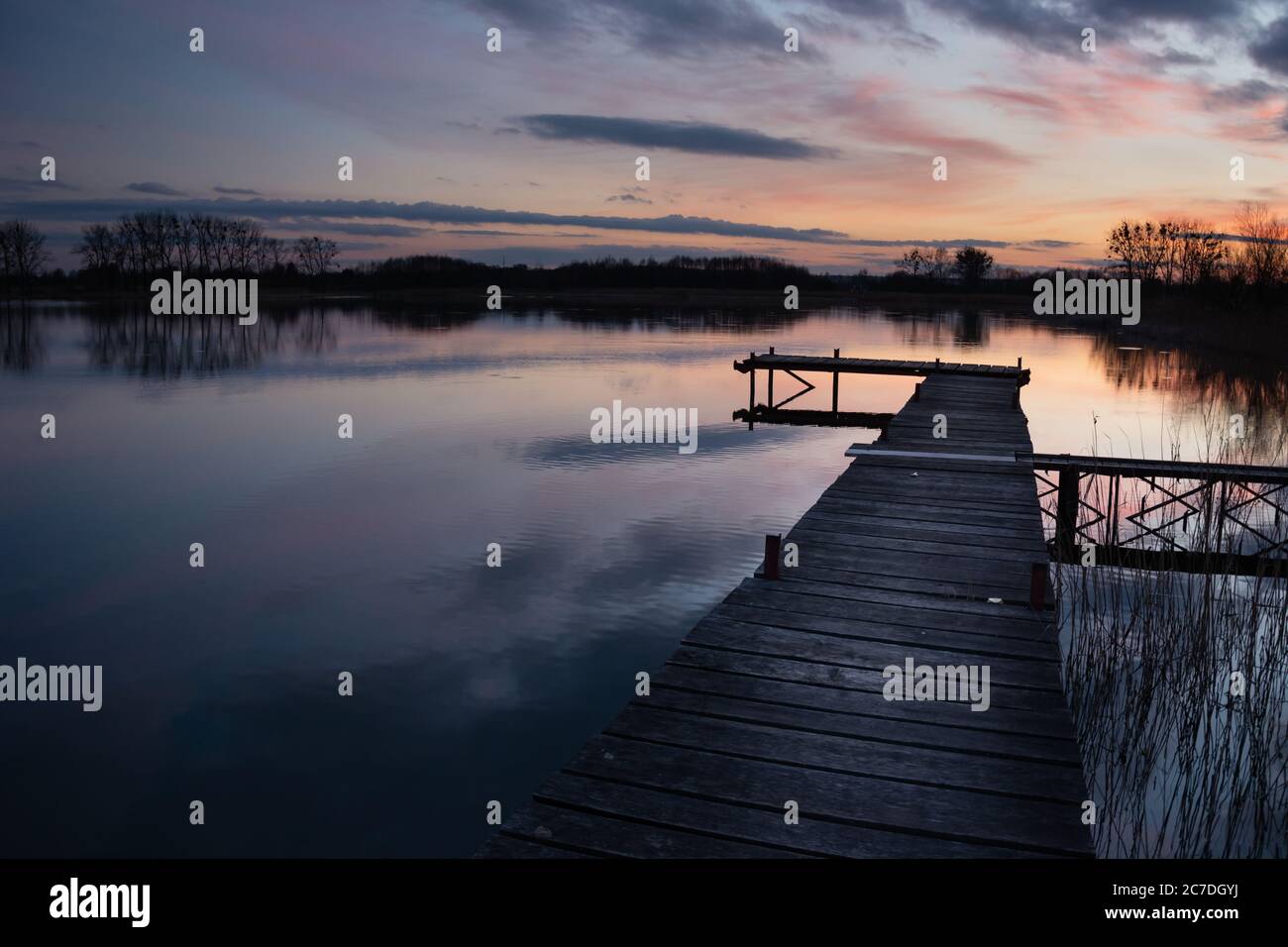 Hölzerner Steg an einem ruhigen See, abends farbige Wolken bei Sonnenuntergang Stockfoto