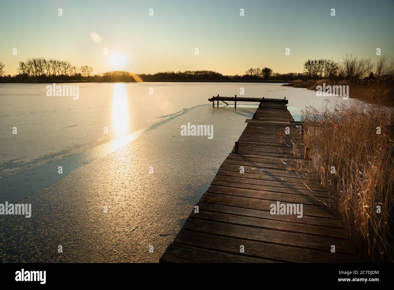 Eine hölzerne Plattform auf einem gefrorenen See und die Sonne über dem Horizont, sonniger Wintertag Stockfoto