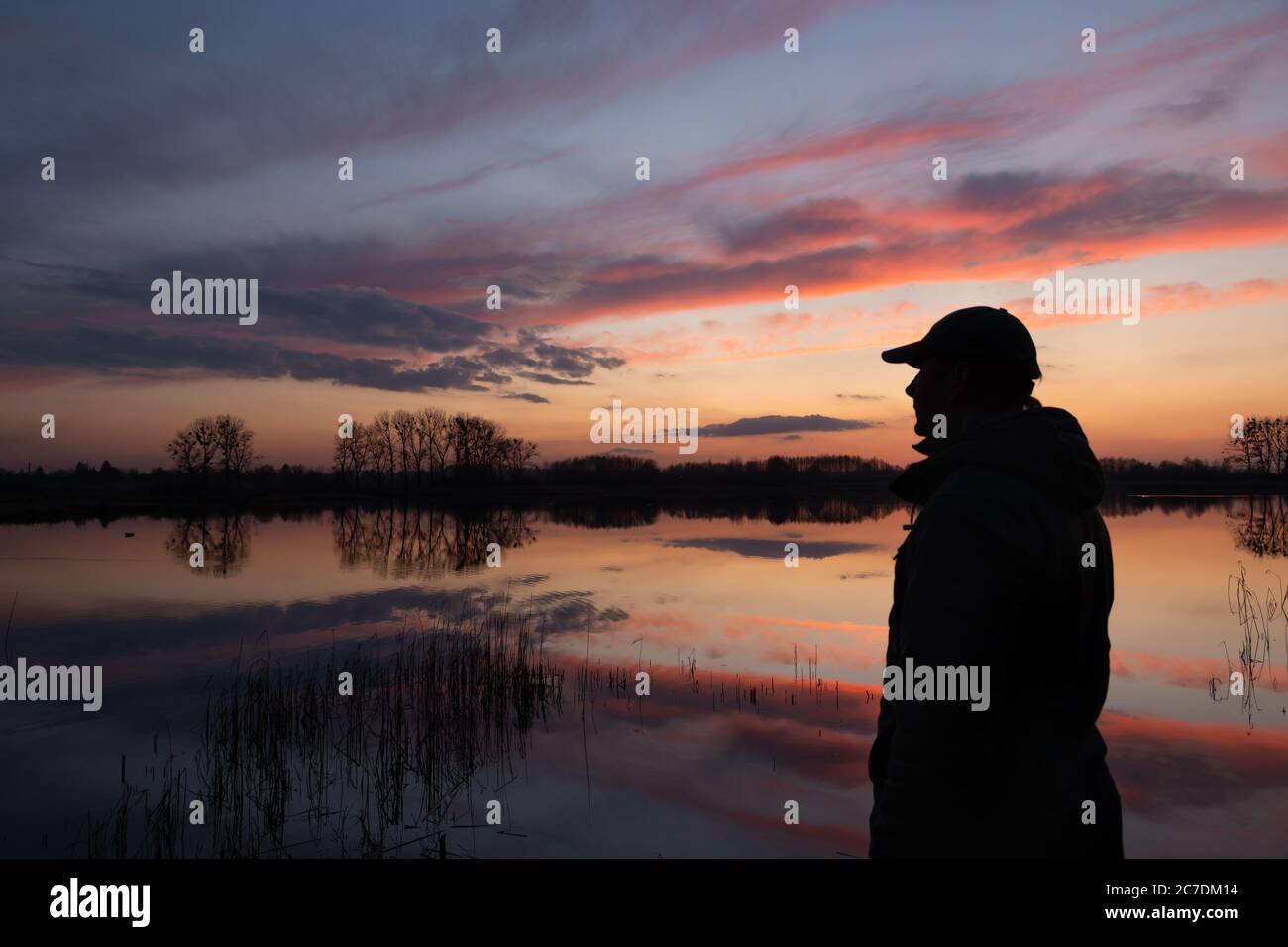 Die Silhouette eines Mannes am Ufer eines Sees und Himmel bei Sonnenuntergang, Frühling Abend Blick Stockfoto