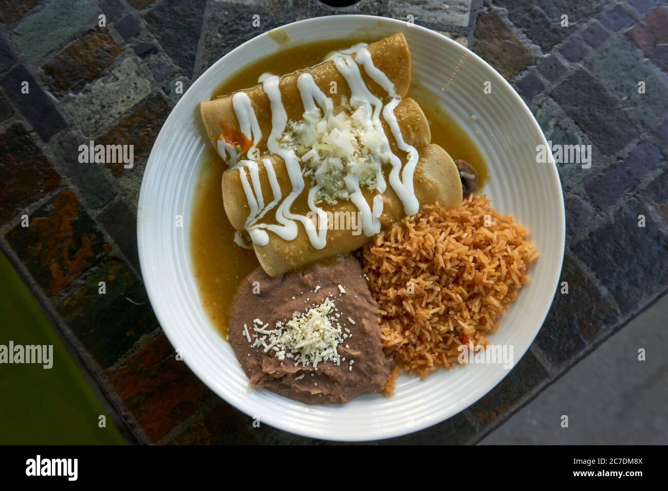 Nahaufnahme eines Tellers mexikanischer vegetarischer Enchiladas mit grüner Tomatillo-Sauce, gebratenen Bohnen und Reis von oben Stockfoto