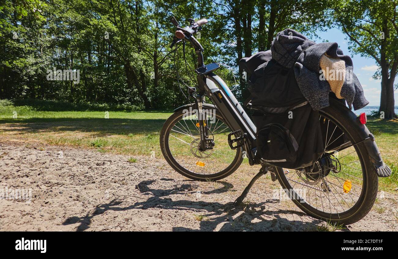 Steinhude, 29. Mai 2020: Elektrofahrrad mit Ladung und angeschlossenem Smartphone zur Navigation steht auf einer Schotterstraße neben einer Wiese. Stockfoto