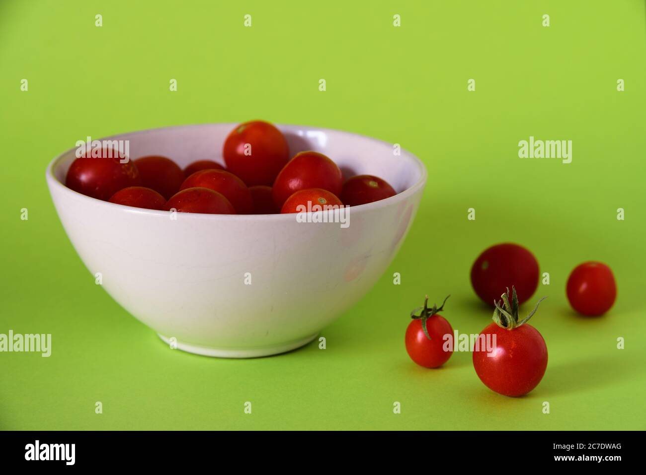 Schließen Sie Schuss von kleinen roten Tomaten in einer weißen Schüssel Und auf einer grünen Oberfläche Stockfoto