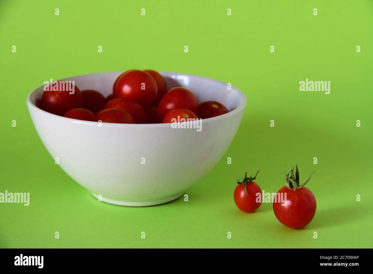 Schließen Sie Schuss von kleinen Tomaten in einer weißen Schüssel auf Eine grüne Oberfläche Stockfoto