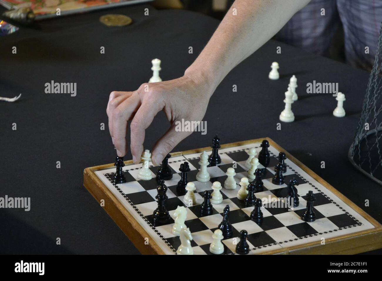 Schachspiel. Hand eines jungen Mannes, der Schachfiguren auf einem Brett mit weißen und schwarzen Figuren auf schwarzem Hintergrund bewegt. Stockfoto