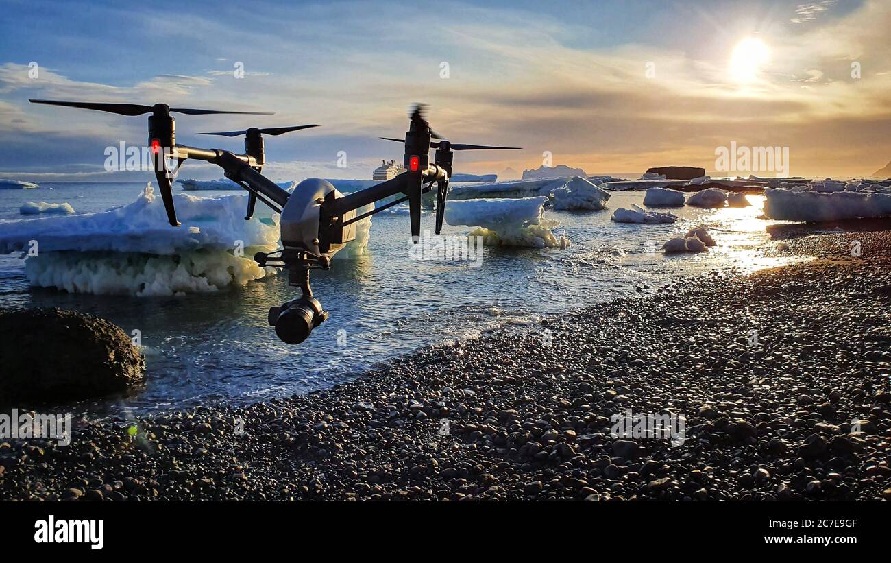 Drohne fliegt unter Sonnenaufgang über einem Kiesstrand mit Eisbergen im Hintergrund Stockfoto