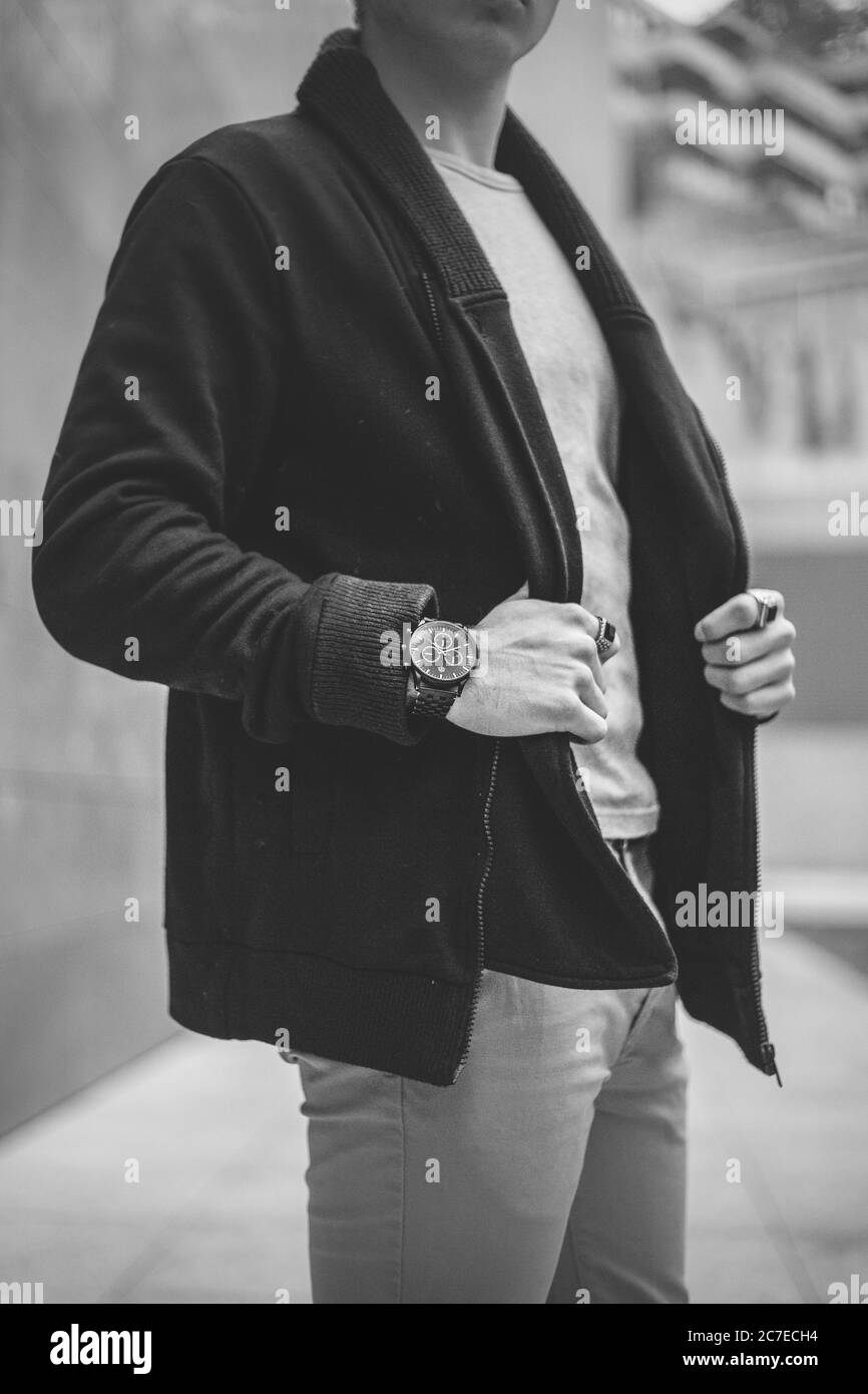 Graustufenaufnahme einer Person mit einer Uhr, die eine trägt Schwarze Jacke und Jeans stehen auf der Straße Stockfoto