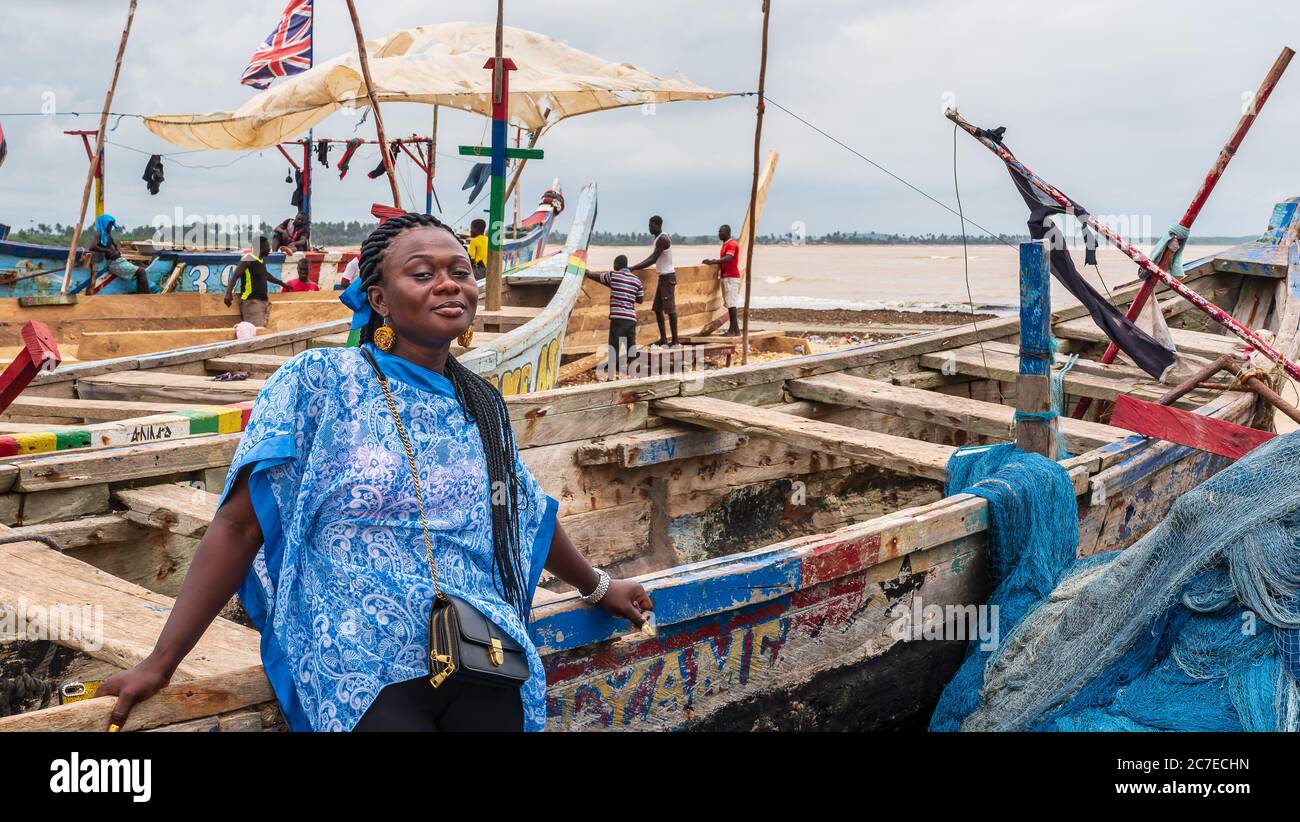 Afrikanische Frau aus Ghana mit blauem Kleid steht bei einem Fischerboot im Fischerdorf Shama Ghana Westafrika 2019 September 15 Stockfoto