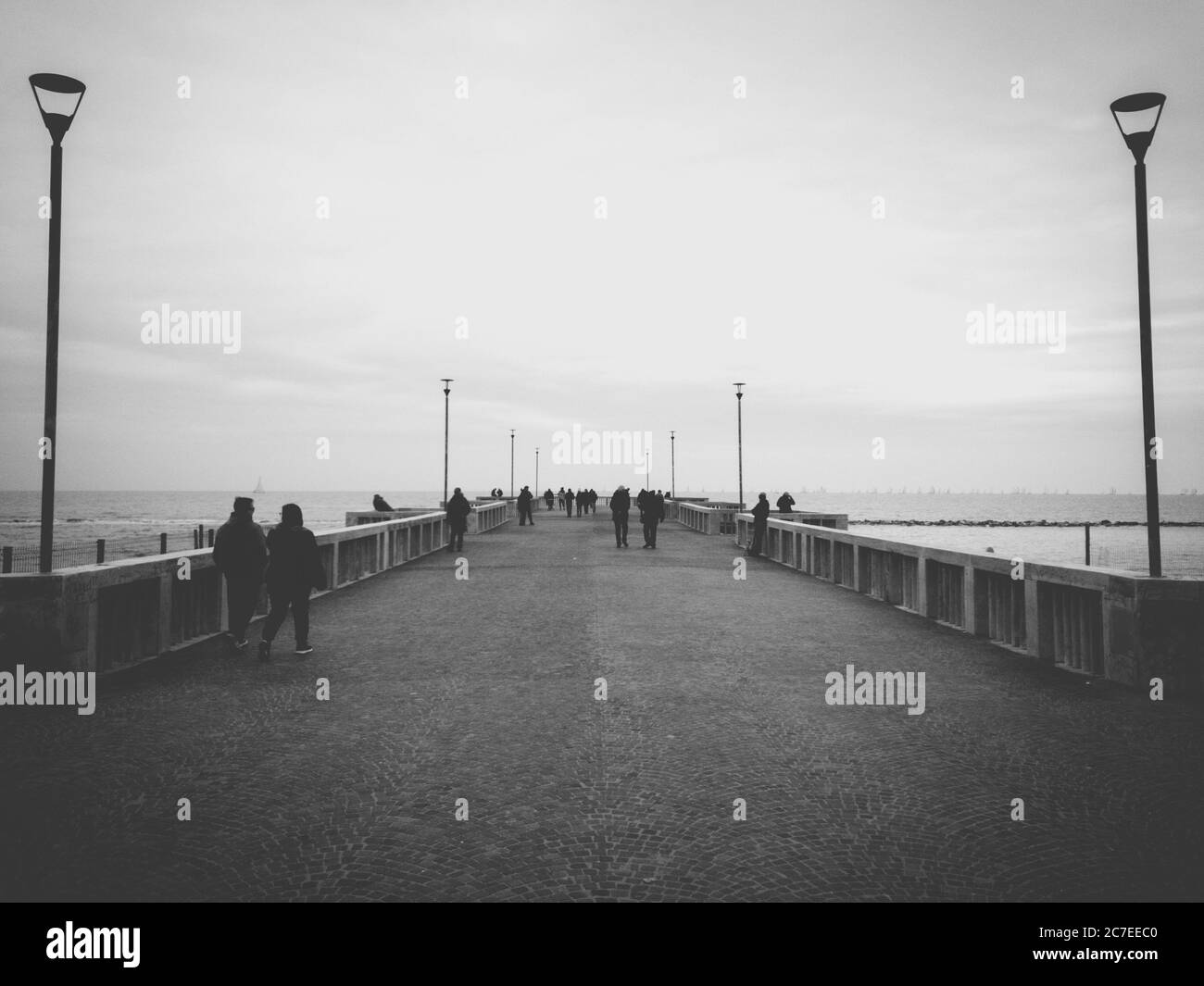 Horizontale Graustufenaufnahme von Menschen, die auf der Brücke in der Nähe stehen Ein See unter dem atemberaubenden Himmel Stockfoto