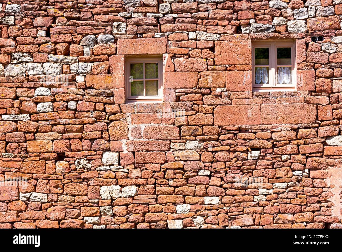 Eine alte rote Sandsteinmauer mit kleinen Fenstern im französischen