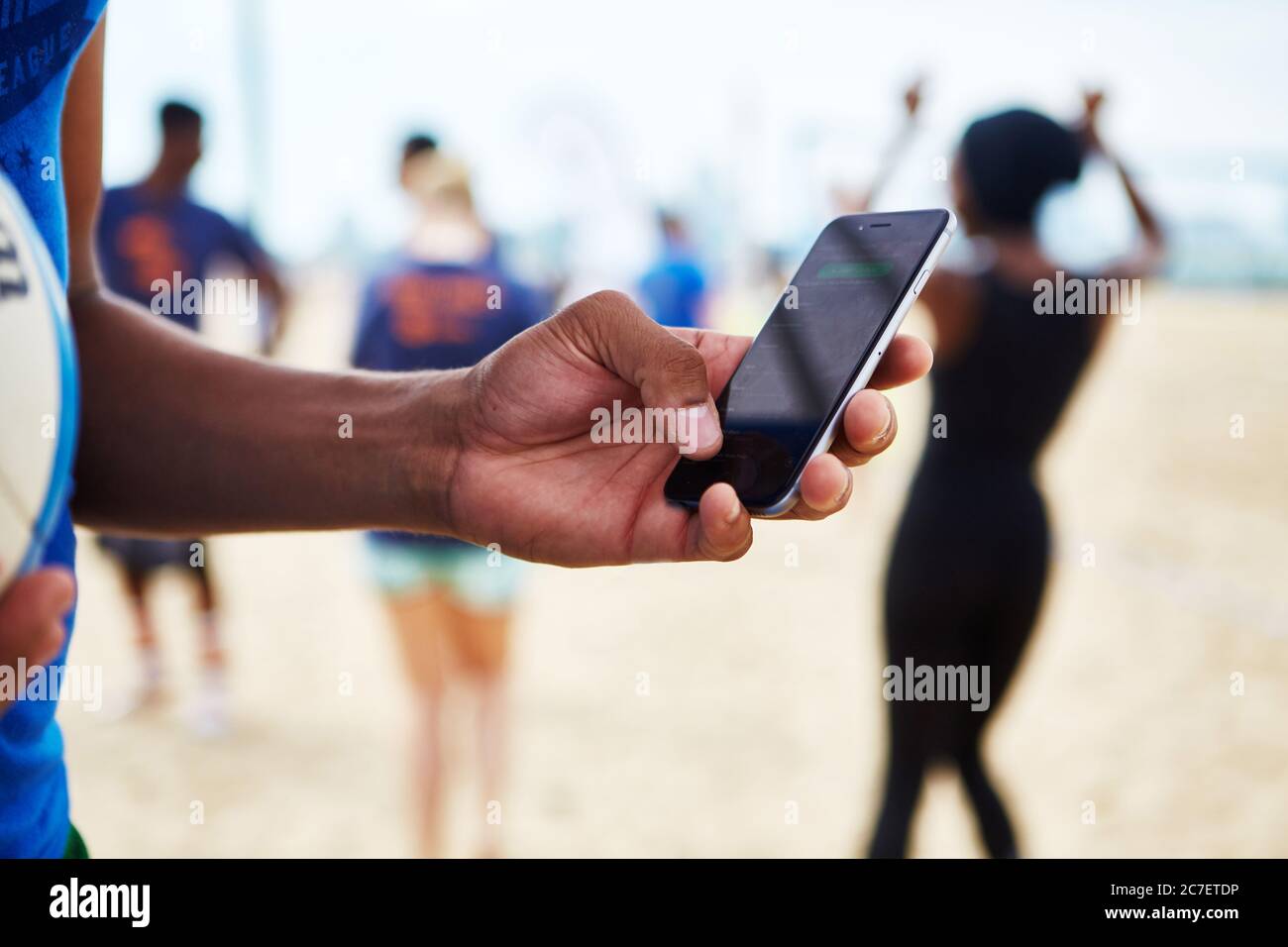 Ein afroamerikanischer Mann passt die Lautstärke auf der Musik bei einer Beachvolleyball-Party im Freien an. Stockfoto