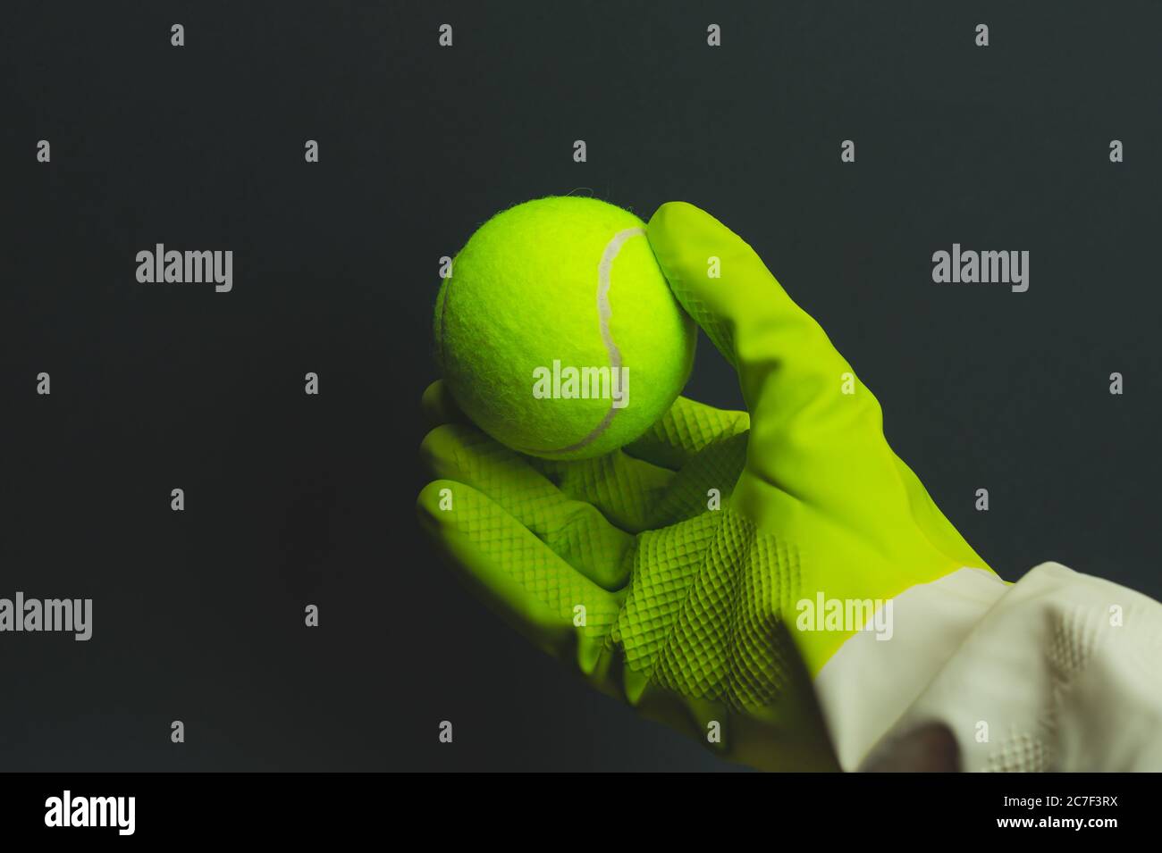 Hand in Schutzhandschuh hält einen gelben Tennisball. In Erwartung der Outdoor-Aktivität Stockfoto