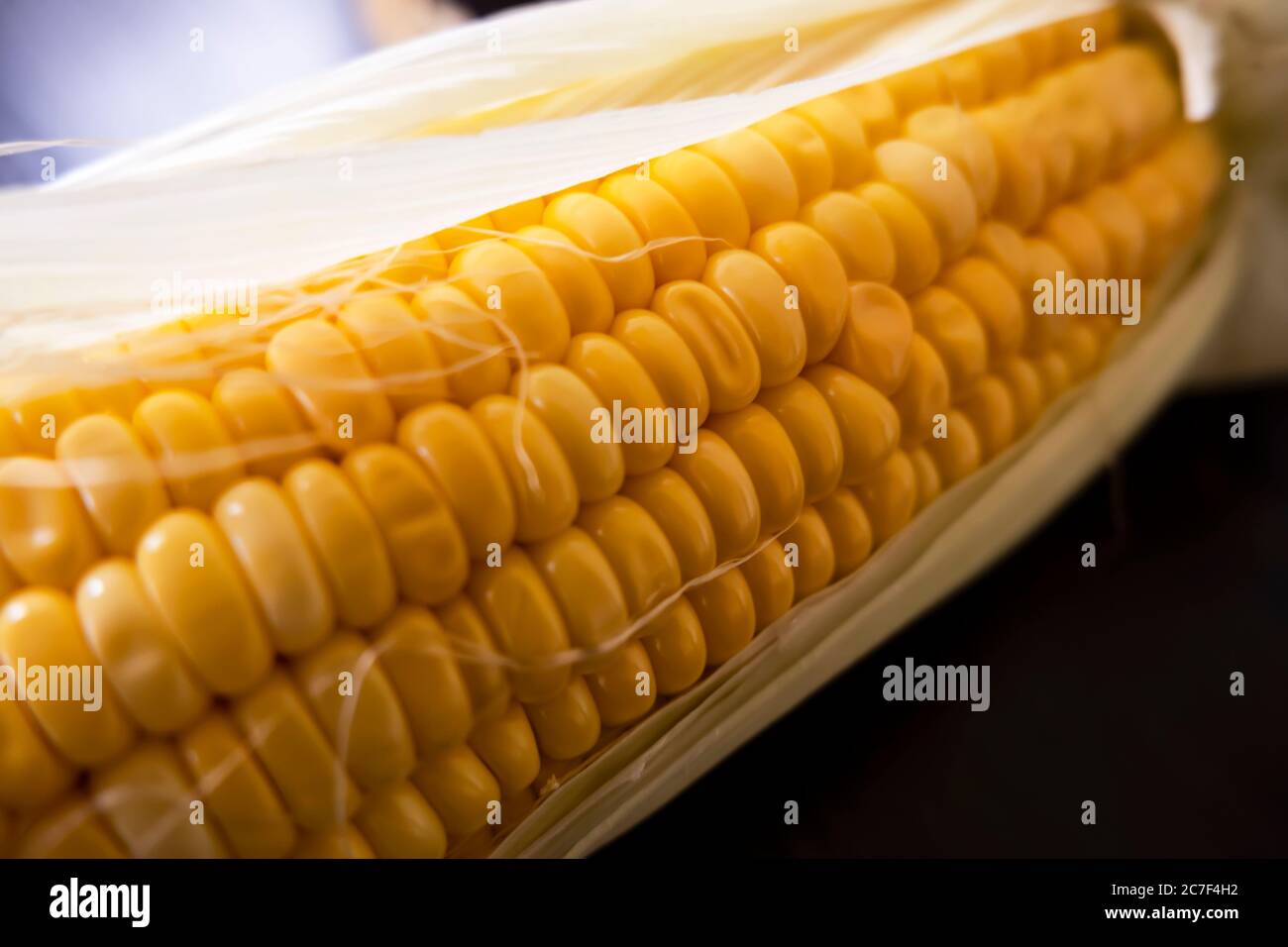 Eine Makroaufnahme von rohen Maiskörnern und -Blättern auf dunklem Hintergrund Stockfoto