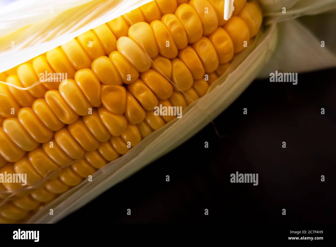 Eine Makroaufnahme von rohen Maiskörnern & Blättern auf Holztisch Stockfoto