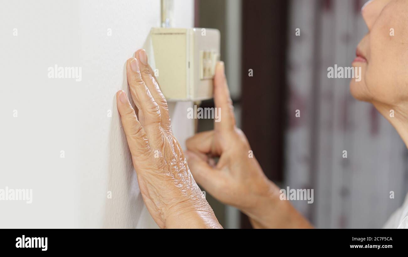 Ältere Frau Hand, die das Licht mit einem Wandschalter anmacht Stockfoto