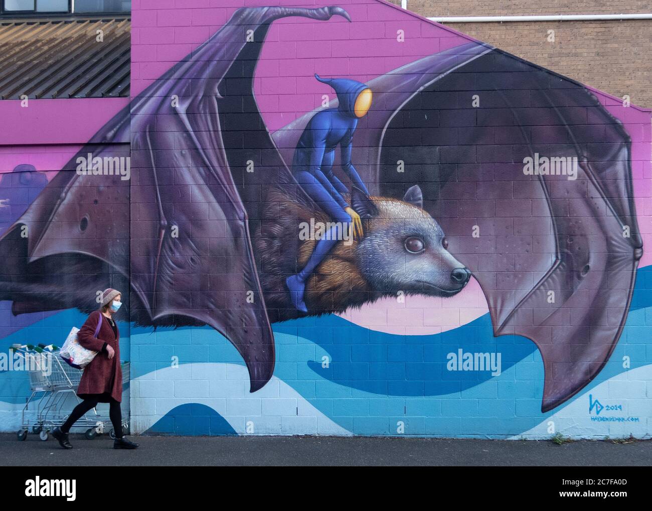 Melbourne Australien Covid-19 Pandemie. Eine Person mit einer schützenden Gesichtsmaske geht an der Street Art einer Fledermaus in Melbourne vorbei. Stockfoto