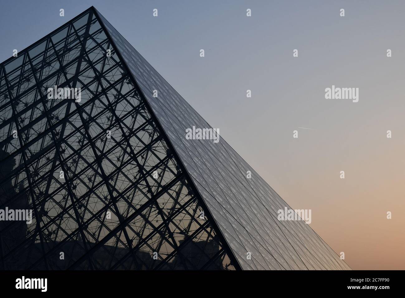 Pyramidenförmige Glaskuppel vor klarem Himmel bei Sonnenuntergang. Futuristische transparente Glas Dachkonstruktion von Dreieck geometrische Form Stockfoto