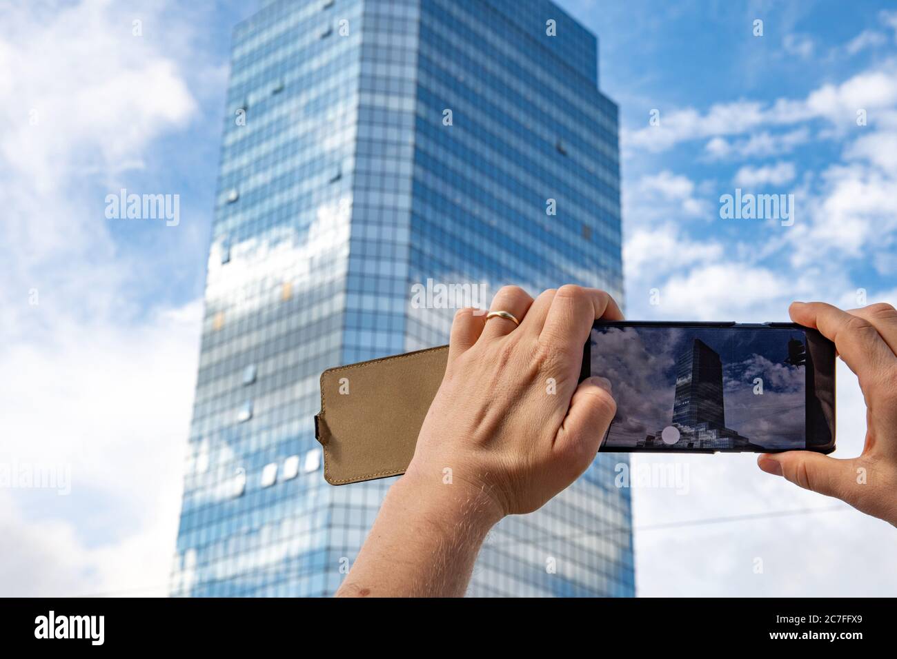 Männliche Hände halten Handy und nehmen Foto von Wolkenkratzer und blauen Himmel mit weißen Wolken. Bild der Stadtlandschaft auf Smartphone-Bildschirm in den Händen des Menschen Stockfoto